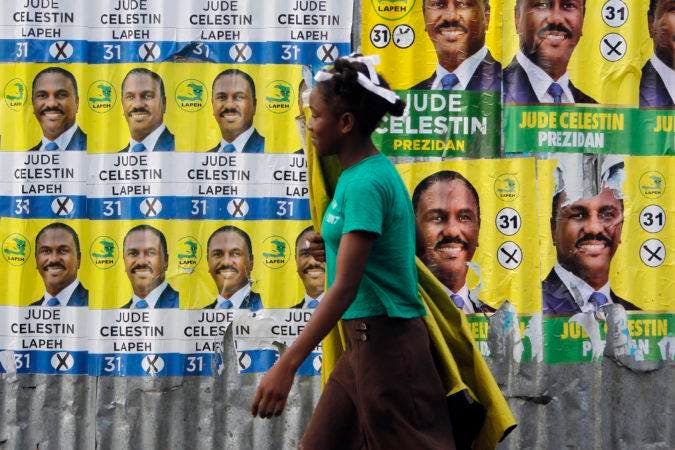 A woman walks past a metal sheeting covered with campaign posters promoting presidential candidate Jude Celestin, in Port-au-Prince, Haiti, Friday, Nov. 18, 2016. Haitians are going to the polls Sunday to pick Haiti's next president. Haiti is holding long-delayed presidential elections Sunday. Last year’s vote was annulled and the nation has been operating with a provisional president since February. (AP Photo/Ricardo Arduengo)