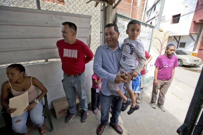 El político opositor Miguel Castillo sostiene a un chico discapacitado de seis años llamado Tomás ante un comedor social impulsado por la oposición, donde el pequeño puede tomar una comida gratis, en Caracas, Venezuela. (AP Foto/Fernando Llano). 