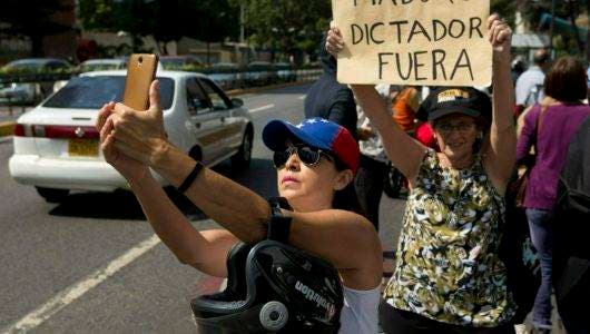 Una miembro de la oposición se toma una selfie junto a una mujer sosteniendo un cartel durante una protesta en Caracas, Venezuela, el viernes 11 de enero de 2019. (AP Foto/Fernando Llano)