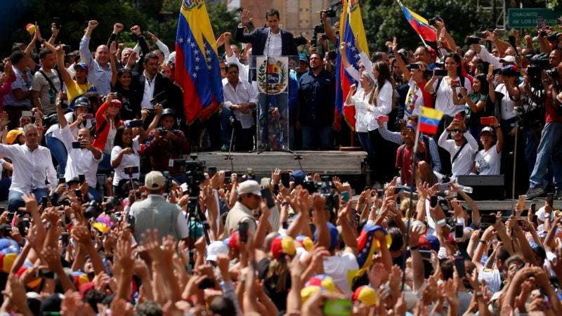 Juan Guaido, head of the opposition-run congress, looks down and holds up his hand during his symbolic swearing-in as interim president of Venezuela on a stage during a rally demanding President Nicolas Maduro's resignation in Caracas, Venezuela, Wednesday, Jan. 23, 2019. Guaido declared himself interim president. (AP Photo/Fernando Llano)