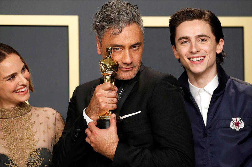 Taika Waititi se aferró a la estatuilla que acababa de ganar por mejor guión adaptado por "Jojo Rabbit", flanqueado por los actores Natalie Portman (izq.) y Timothee Chalamet (der.) quienes le entregaron el galardón.