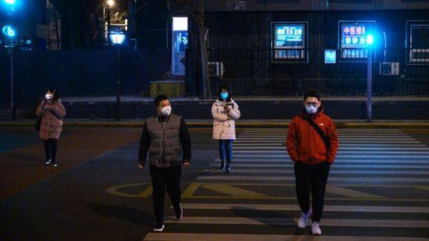 Cuatro personas cruzan una calle en China con máscaras. 