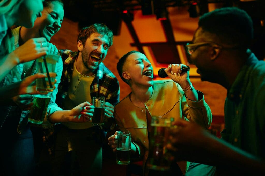 cheerful friends having fun while singing karaoke during their night out in a pub